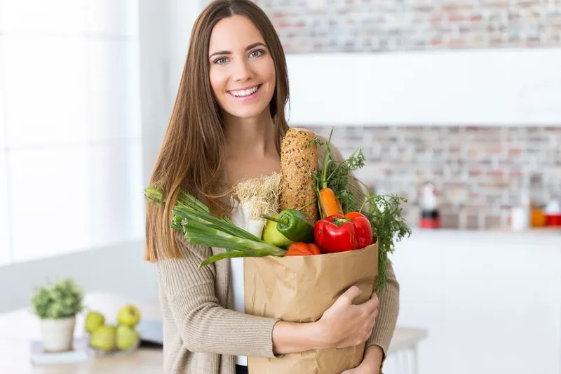 mulher alegre segurando um cesto de vários alimentos saudáveis em uma cozinha