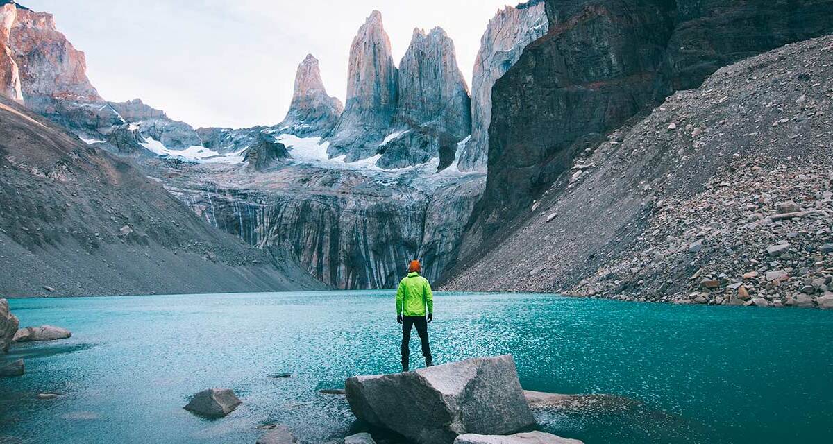 Homem em frente a um lago da Patagônia, olhando as montanhas congeladas 